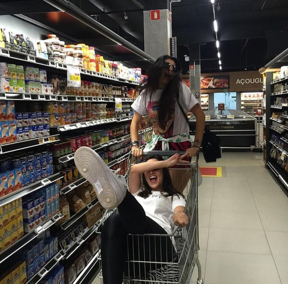 Two teenage friends riding around in a grocery store trolley